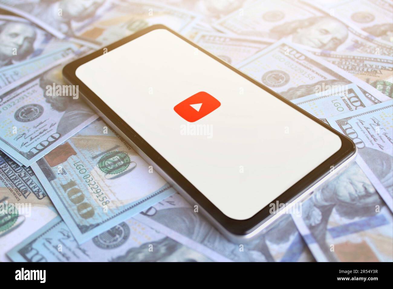 Logo YouTube visualizzato sullo smartphone in cima a una pila di denaro. Concetto di profitto aziendale e monetizzazione Foto Stock