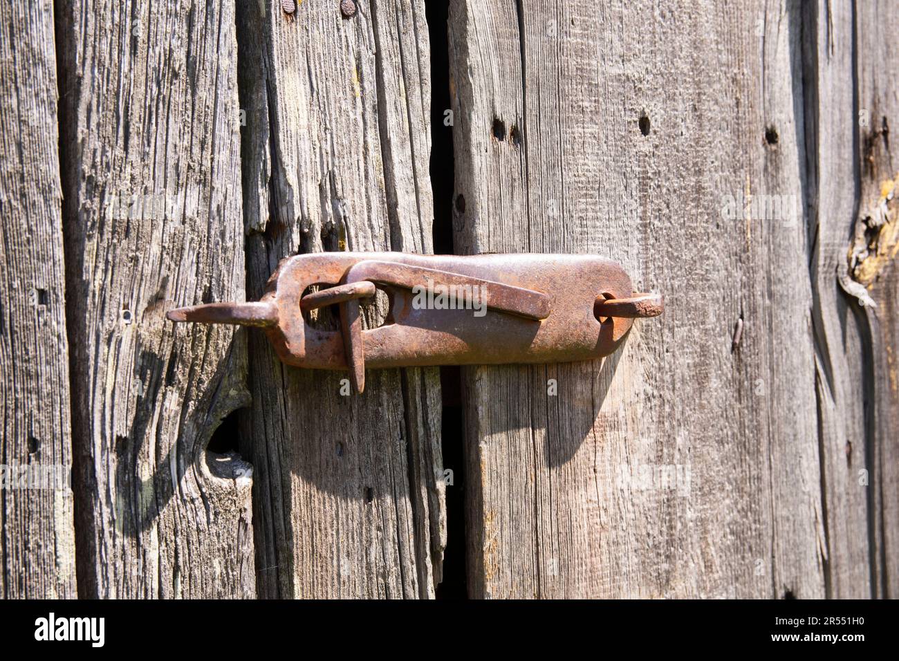 Un vecchio, originale pomolo porta su una secolare porta fienile in legno nel duro pomeriggio sole. Foto Stock