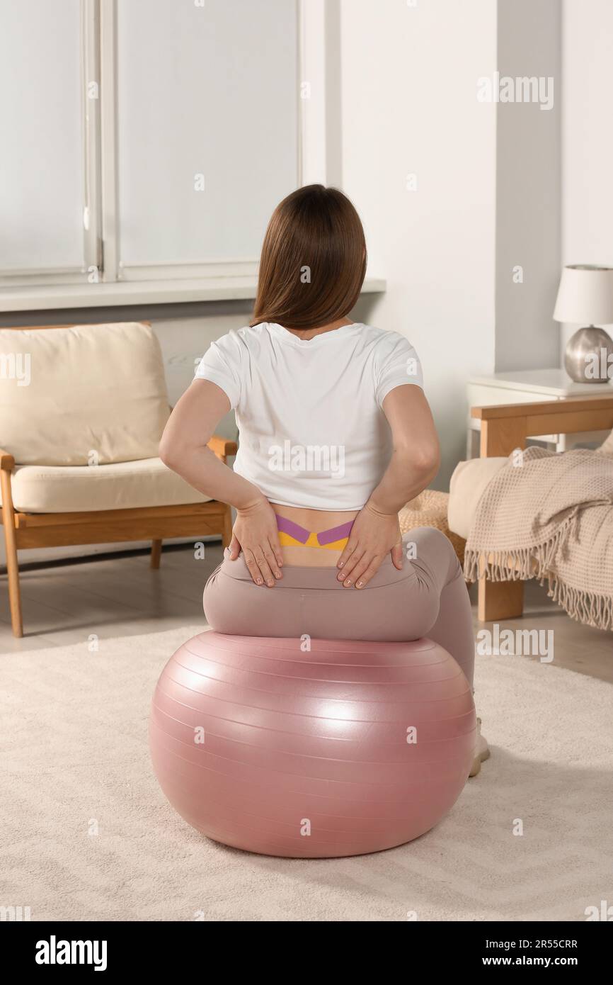 Donna incinta con cinesio nastri fare esercizi su fit ball a casa, vista posteriore Foto Stock