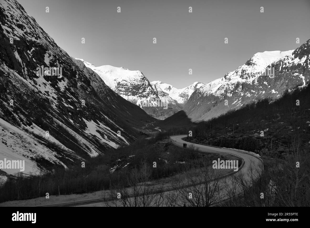 Vista tra le montagne della Norvegia, attraverso la quale una strada conduce in bianco nero. Neve sulle montagne. Paesaggio girato da nord in Scandinavia Foto Stock