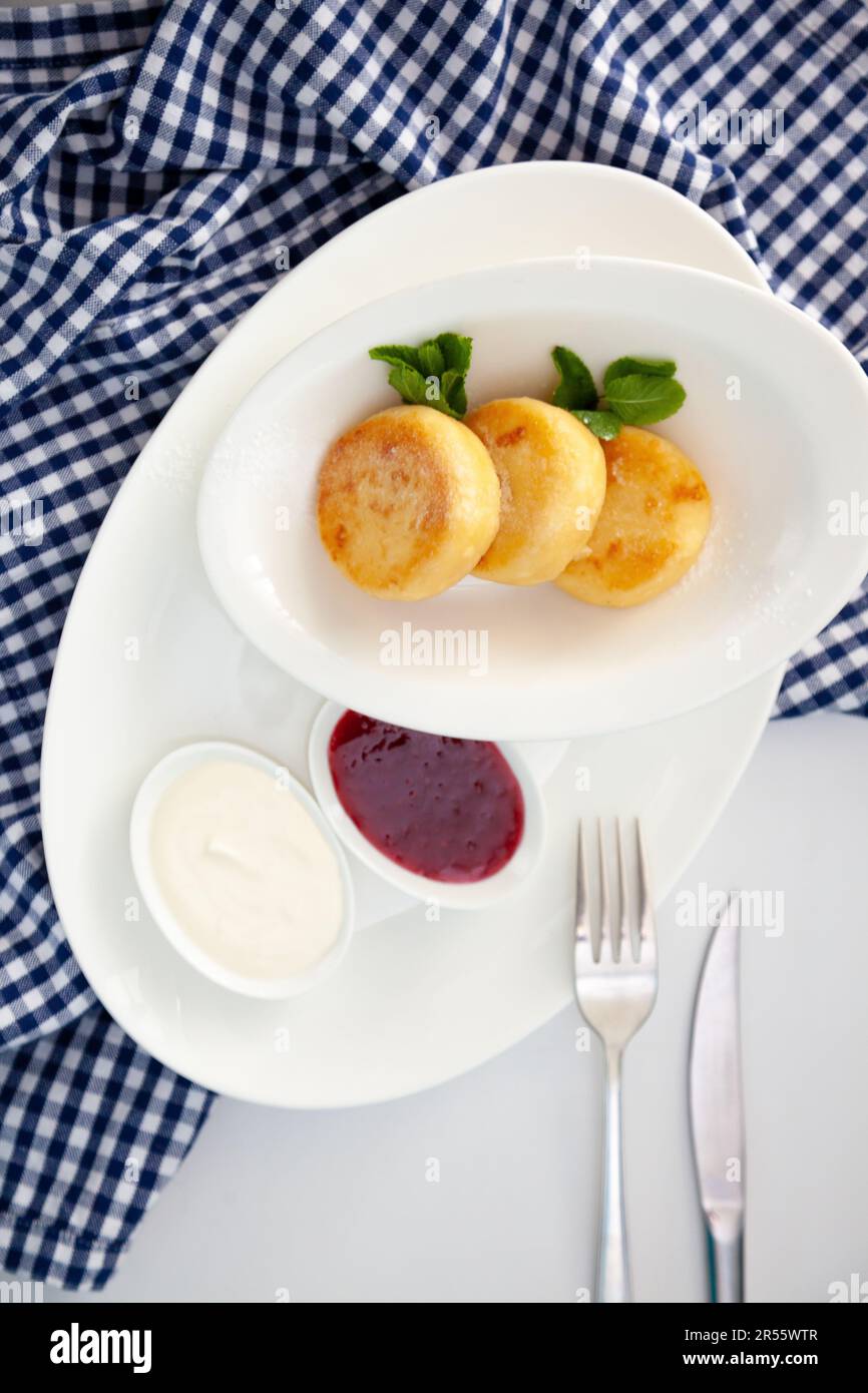 Frittelle di formaggio ricotta rotonda in un piatto bianco su sfondo blu. Cibo prima colazione. Cibo sano. Salsa di panna acida e menta. Primo piano vista dall'alto. Pasto dessert. Frittelle di ricotta al formaggio ricotta. Foto Stock