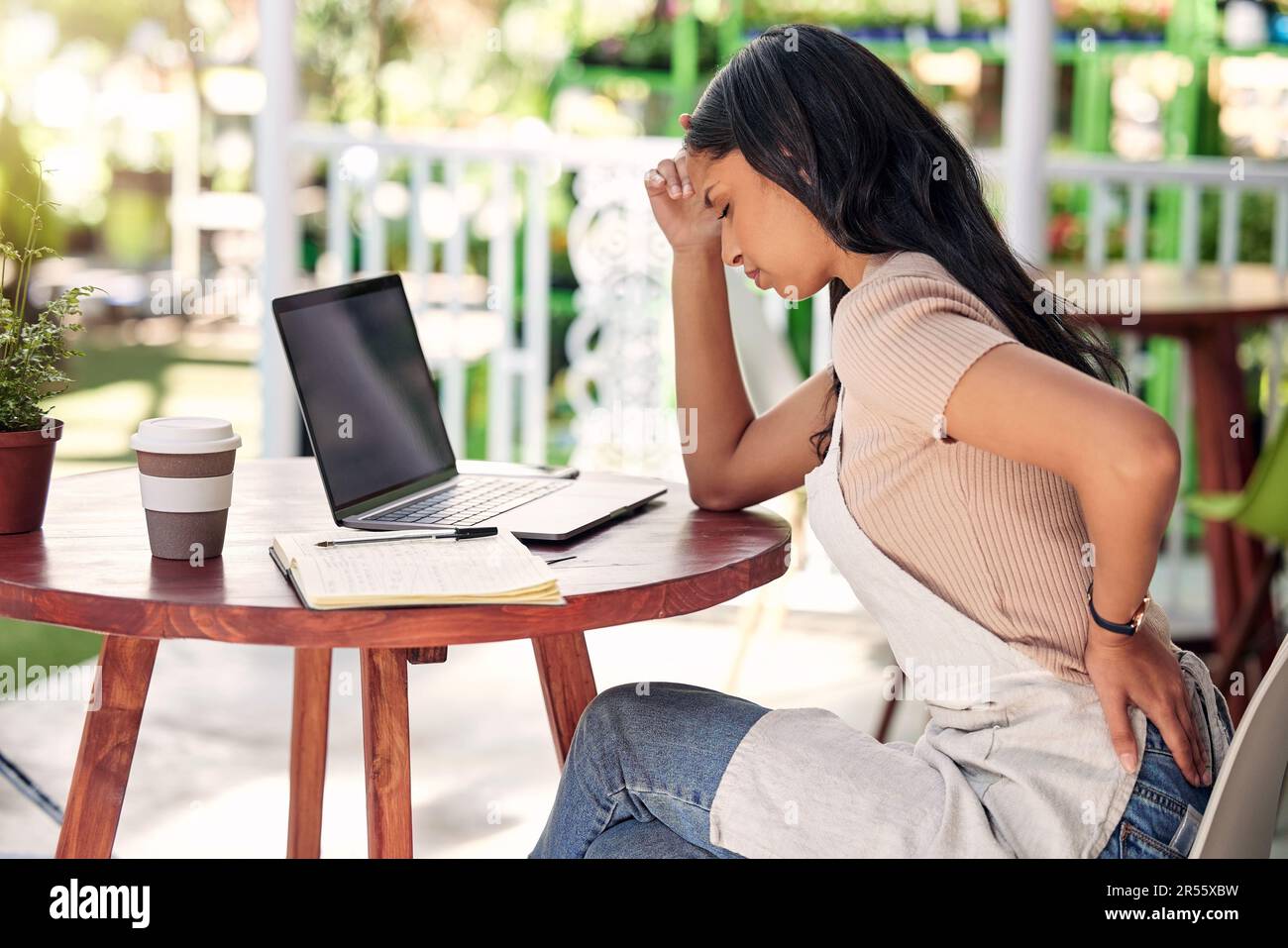 Donna in difficoltà con il computer portatile al tavolo da giardino, bar all'aperto o negozio di piante con stress, burnout e mal di schiena. Salute mentale, proprietario di piccola impresa e. Foto Stock