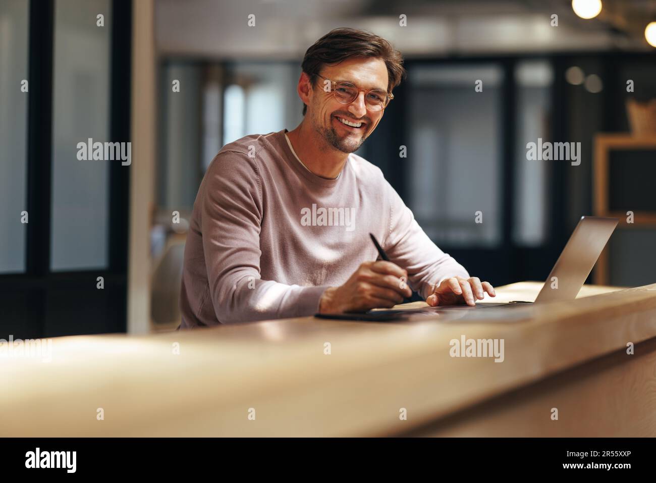 Design grafico professionale sorridente alla macchina fotografica in un bar. Uomo d'affari creativo che lavora con un tablet grafico e un notebook. Design maschile lavoro r Foto Stock
