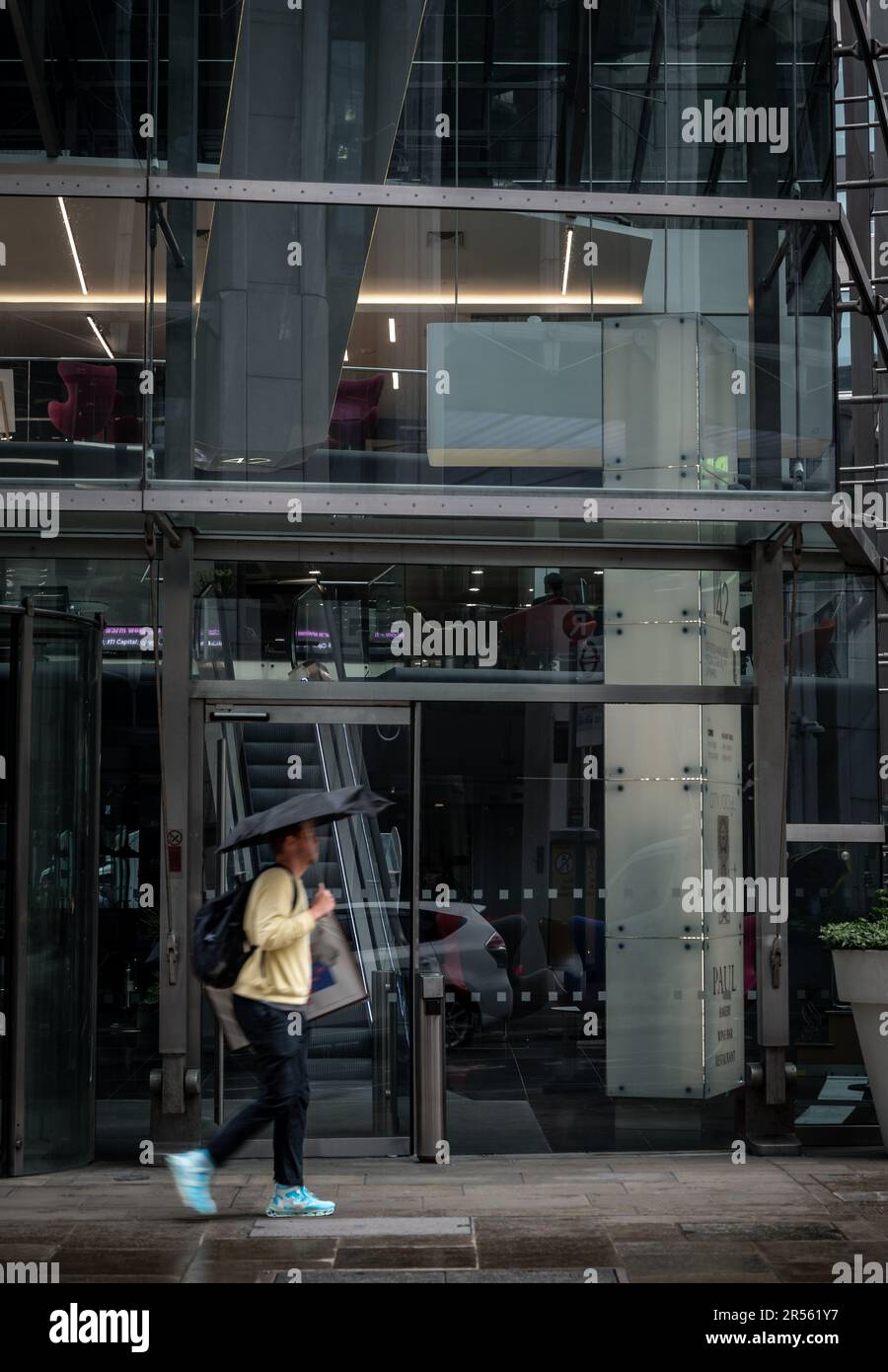 Londra, Regno Unito: Un uomo cammina lungo una strada sotto la pioggia portando un ombrello. Old Broad Street nella città di Londra. Foto Stock