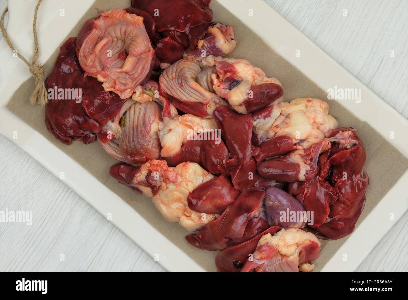 Gibletti di pollo crudi su un asse di ceramica. Gli stomachi di pollo, i cuori e i fegati sono preparati per cucinare. Foto Stock