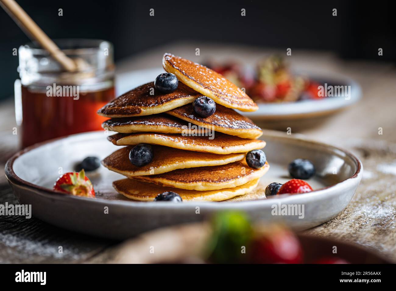 Pancake americani con mirtilli, fragole e ciliegie con salsa di miele. Posto su un piatto rustico di design, su un tavolo rustico in legno. Foto Stock