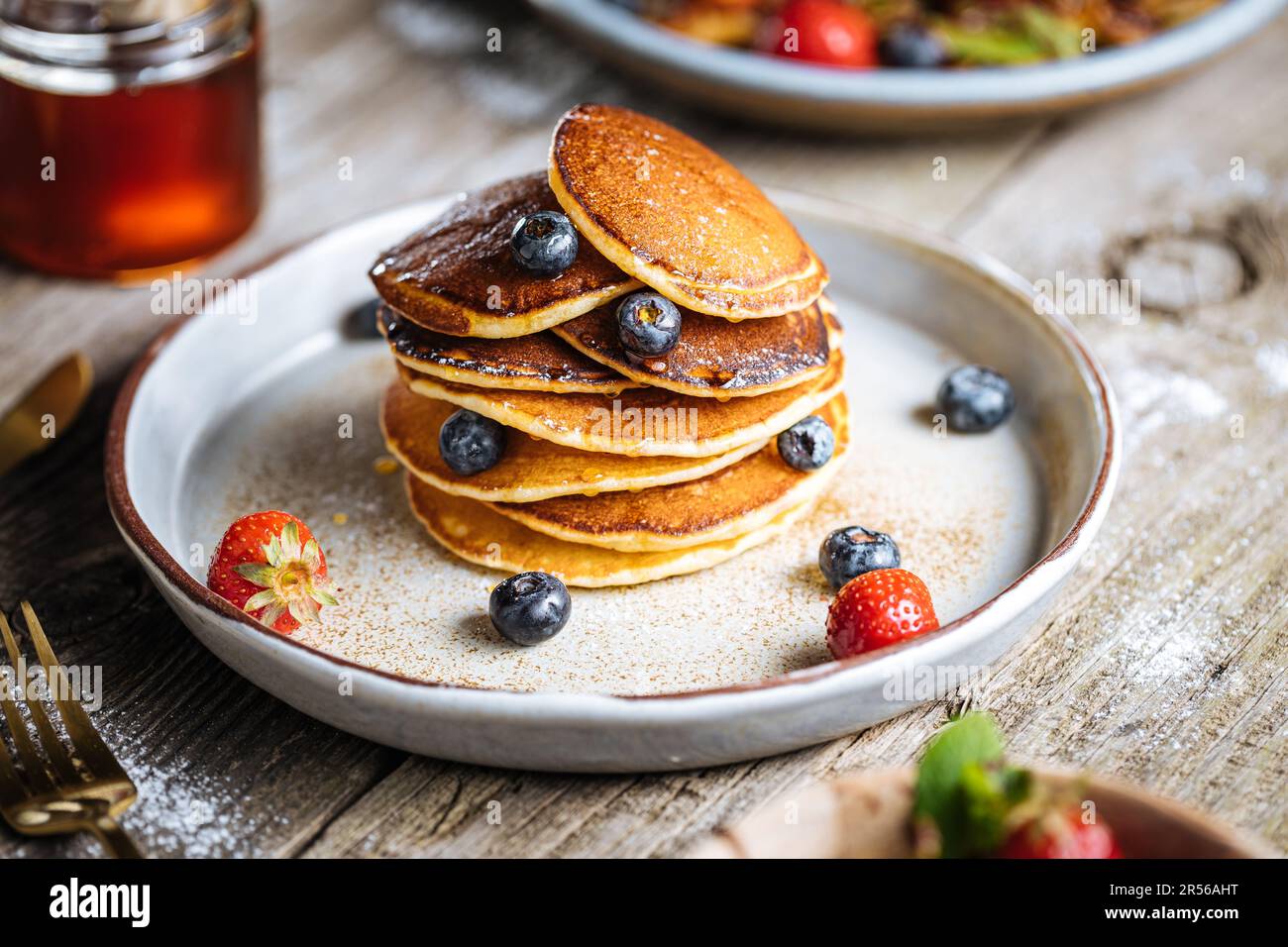 Pancake americani con mirtilli, fragole e ciliegie con salsa di miele. Posto su un piatto rustico di design, su un tavolo rustico in legno. Foto Stock