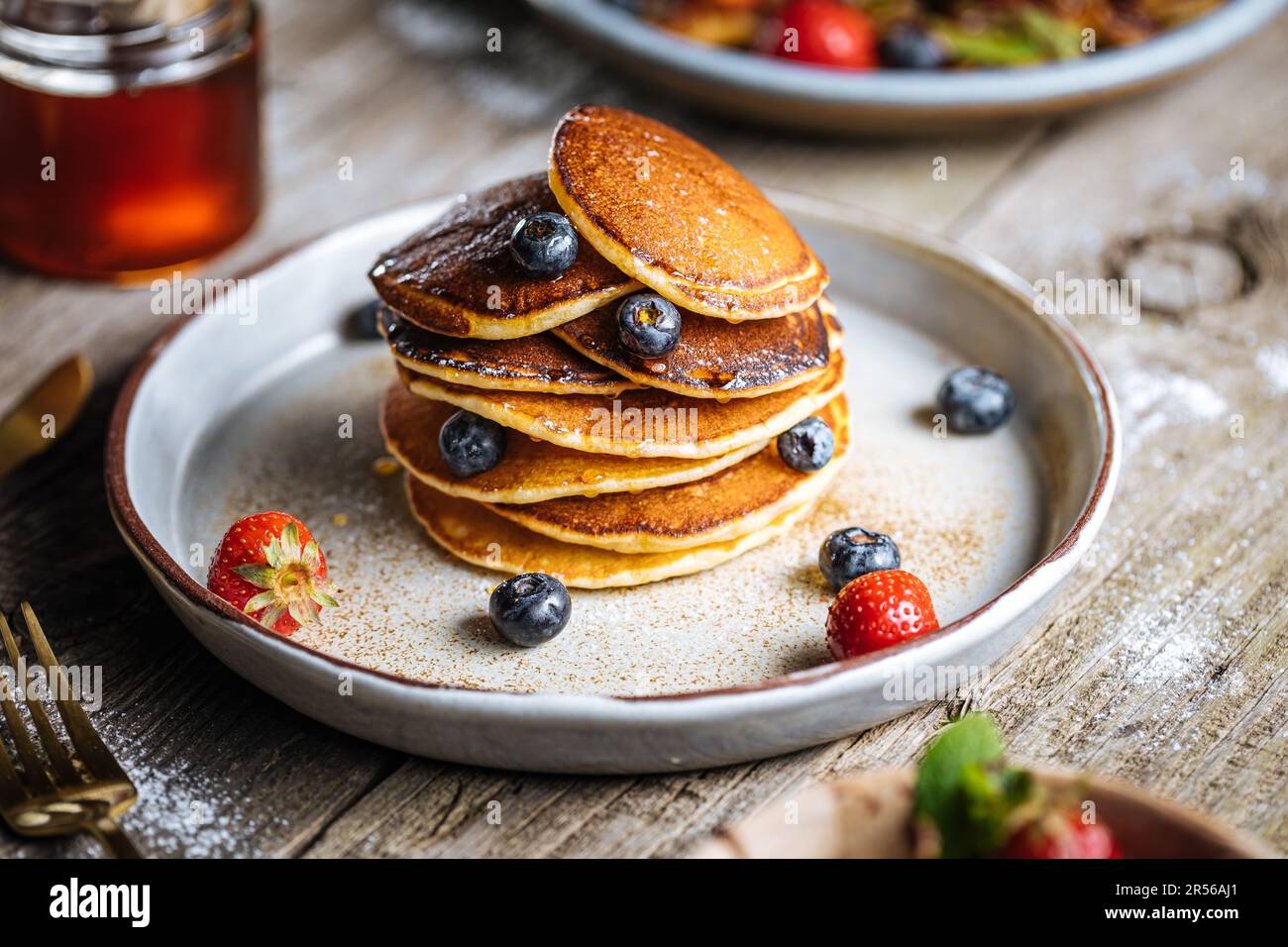 Pancake americani con mirtilli, fragole e ciliegie con salsa di miele. Posto su un piatto rustico di design, su un tavolo rustico in legno. Foto Stock