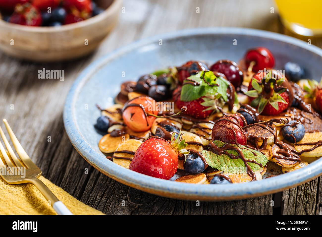 Piccoli pancake americani mescolati con frutta di stagione come fragole, mirtilli e ciliegie. Ricoperto di cioccolato fuso, posto su un legno rustico Foto Stock