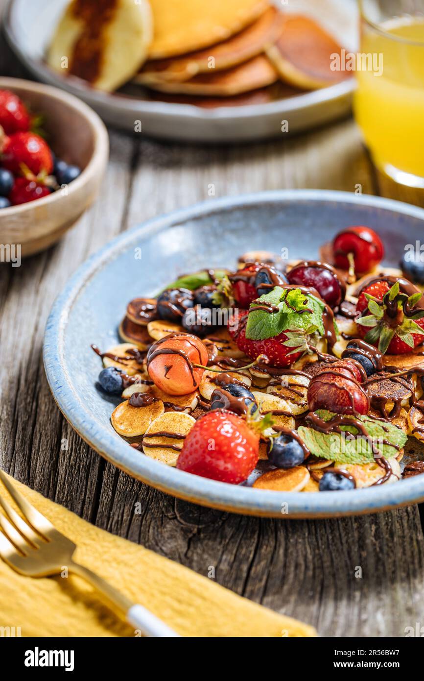 Piccoli pancake americani mescolati con frutta di stagione come fragole, mirtilli e ciliegie. Ricoperto di cioccolato fuso, posto su un legno rustico Foto Stock