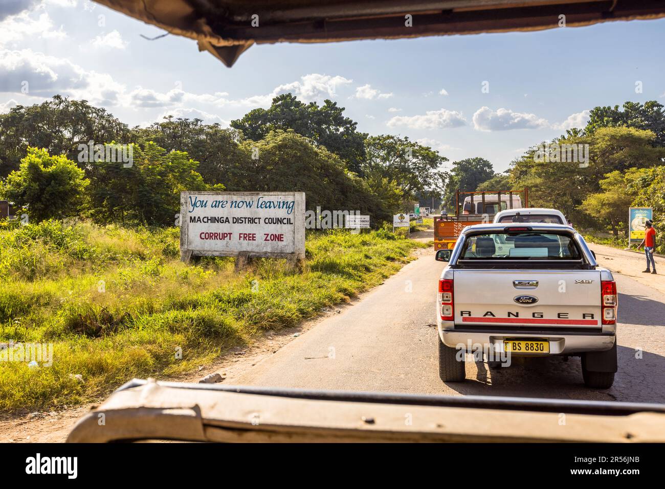 Un cartello ai margini della città promuove la "Zona Libera dalla Corruzione" del Consiglio del Distretto di Machinga nel Malawi; un pick-up aspetta sulla strada in primo piano. Foto Stock