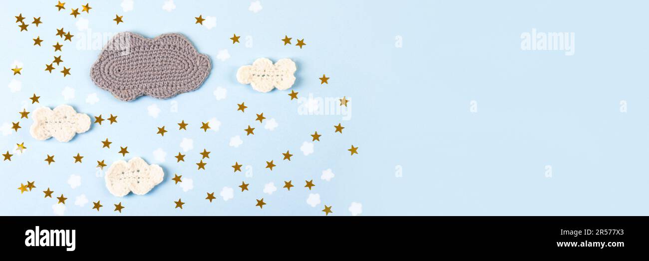 Giocattoli a maglia nuvole e stelle gialle su sfondo blu. Articoli e accessori per bambini. Vista dall'alto, piano di posa, banner Foto Stock