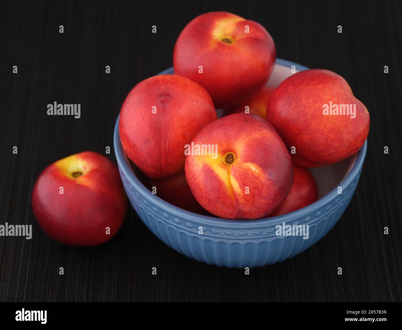 Nettarine raccolte di recente in una ciotola blu su un tappetino nero. Tasto basso. Primo piano. Foto Stock