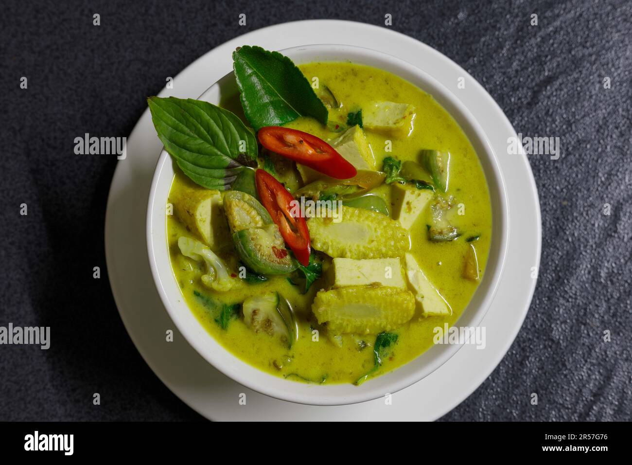 Zuppa di tofu al curry verde. Zuppa di curry verde tailandese in un recipiente bianco su un piatto bianco con fondo scuro. Giacitura piana, sovratesta Foto Stock