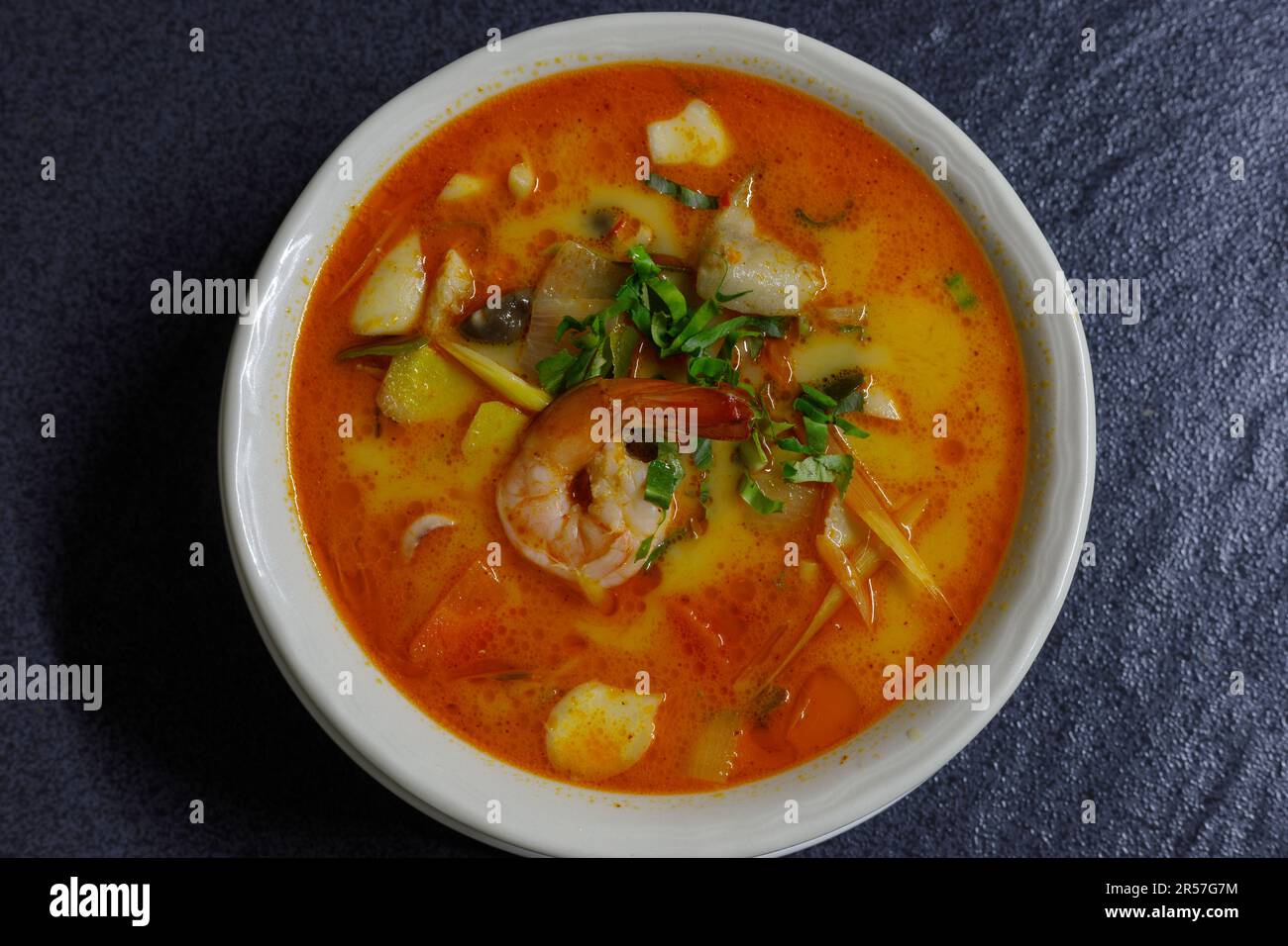Zuppa di pesce Tom Yum in un recipiente bianco su sfondo scuro. Giacitura piana, sovratesta Foto Stock