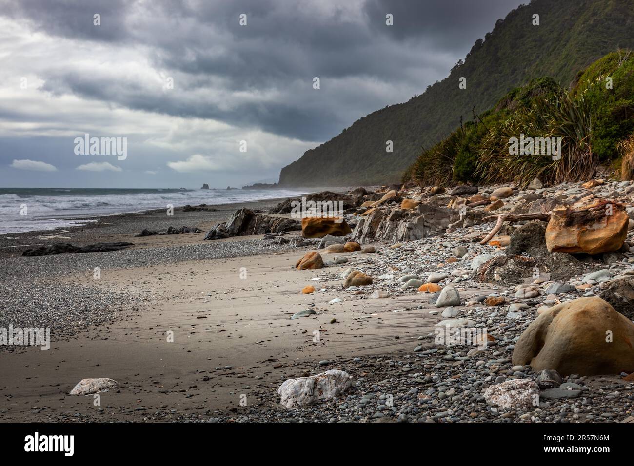 Le tempeste che si avvicinano ad un rock disseminata spiaggia in Nuova Zelanda Foto Stock