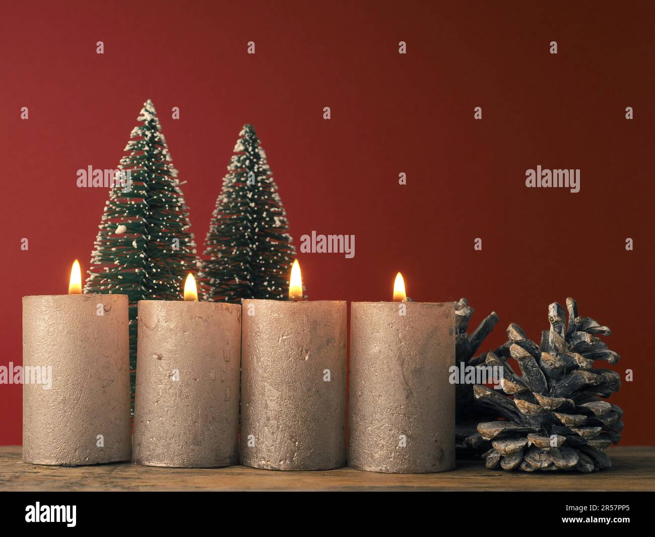 Quattro candele dell'Avvento che bruciano su sfondo rosso con decorazione di Natale Foto Stock