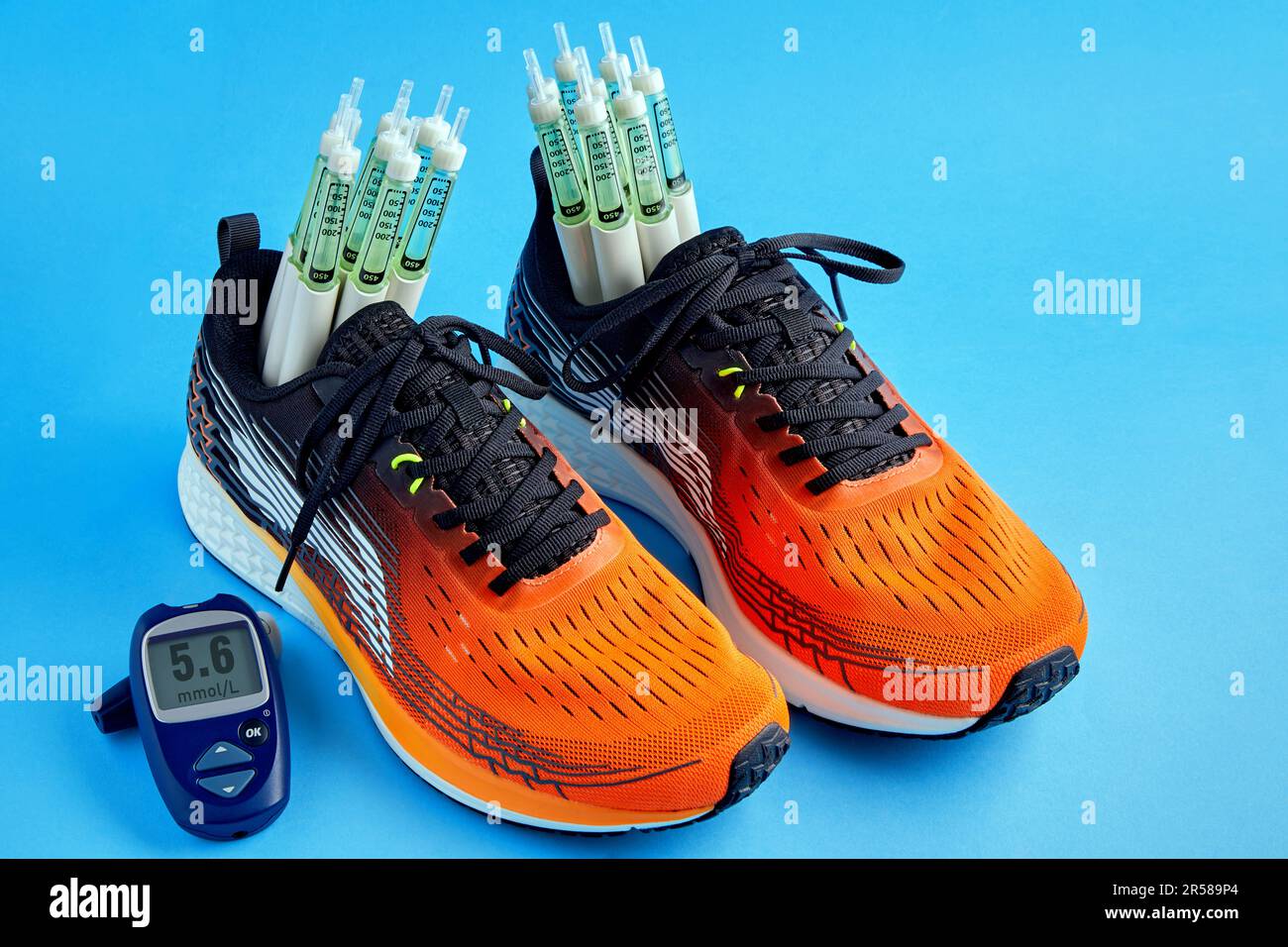 Scarpe da running arancioni con penne per siringa per insulina e un glucometro per la misurazione dello zucchero nel sangue su sfondo blu Foto Stock