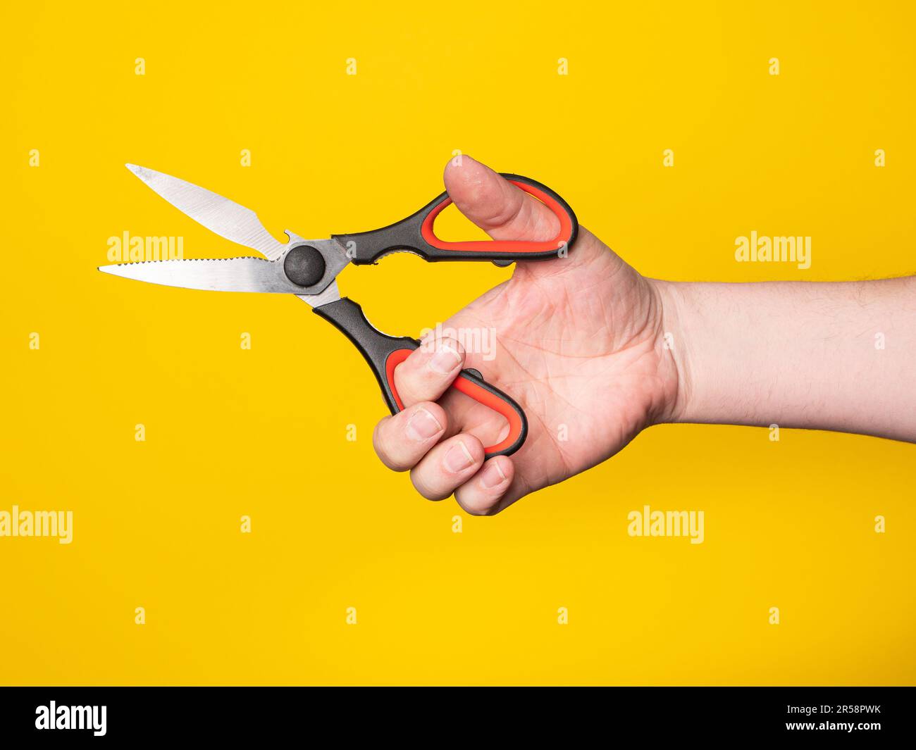 Una mano tiene una forbice. Senza volto, sfondo giallo. Foto Stock