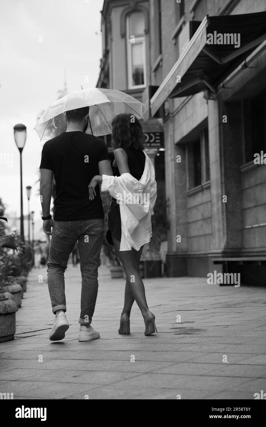 Giovane coppia con ombrello che si gode il tempo insieme sotto la pioggia  sulla strada della città, vista sul retro. Effetto bianco e nero Foto stock  - Alamy