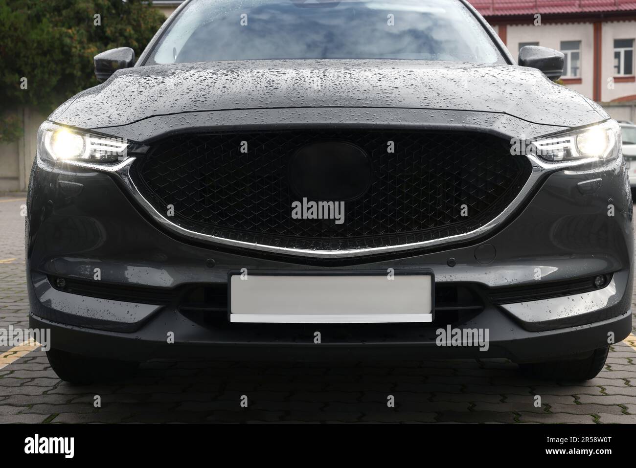 Auto nera con fari accesi in gocce d'acqua parcheggiate all'aperto Foto Stock