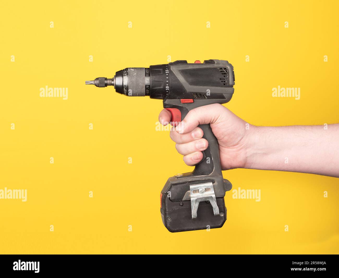 Una mano contiene un cacciavite a batteria. Nessuna faccia, sfondo giallo, spazio di copia. Foto Stock