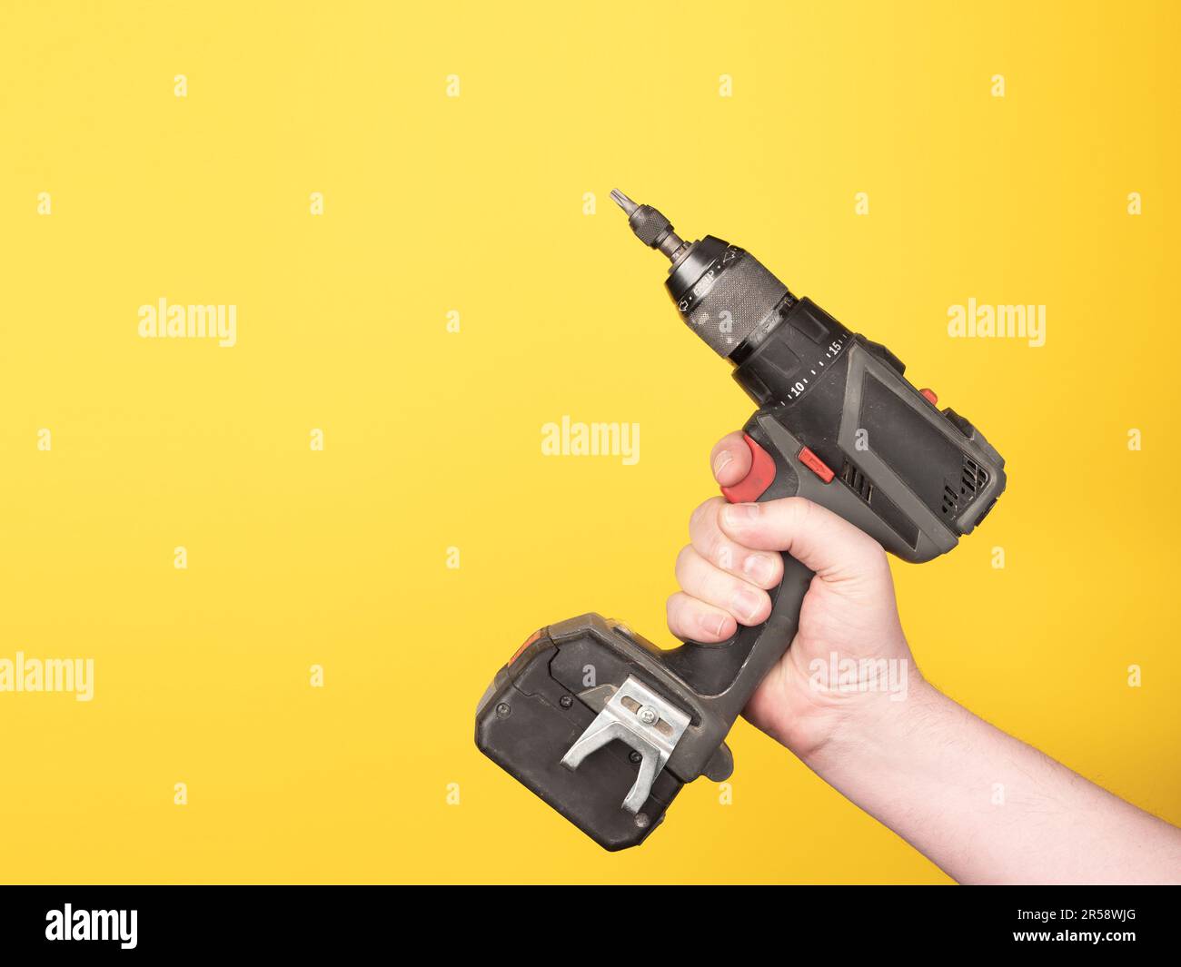Una mano contiene un cacciavite a batteria. Nessuna faccia, sfondo giallo, spazio di copia. Foto Stock