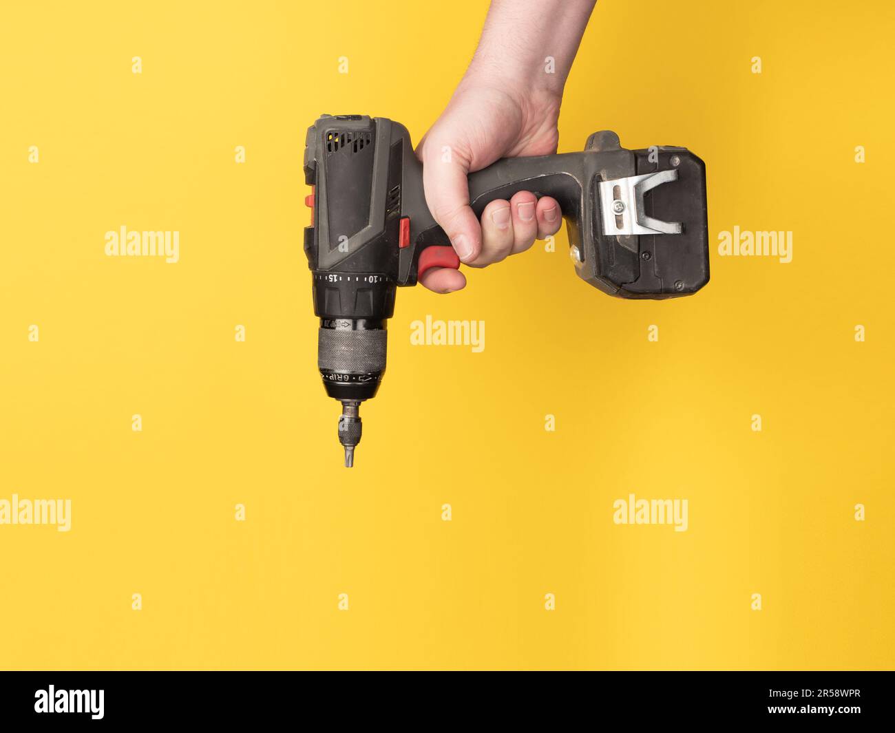 Una mano contiene un cacciavite a batteria. Nessuna faccia, sfondo giallo, spazio di copia. Foto Stock