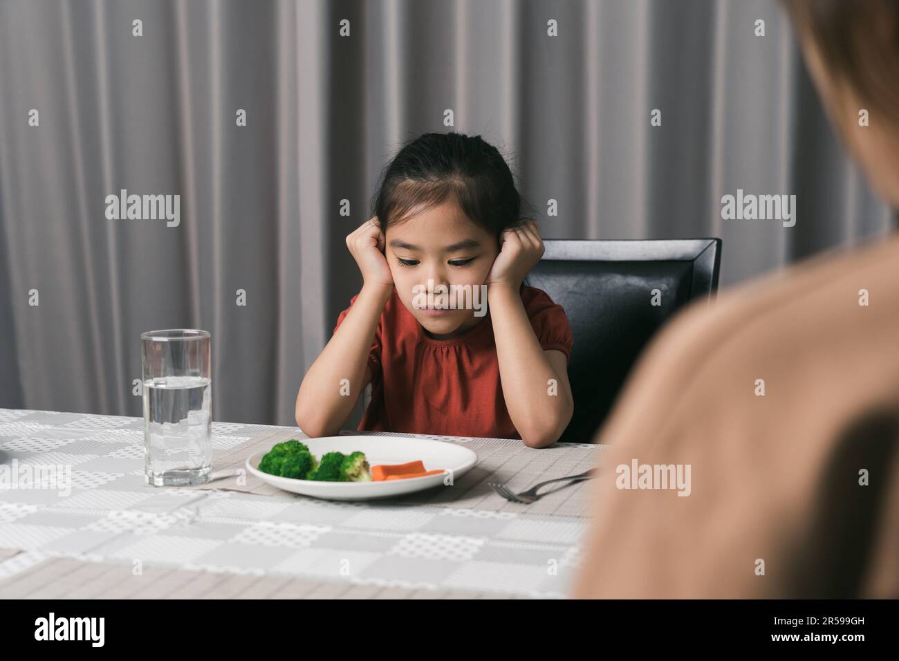 La madre sta dicendo al suo capretto carino mangiano le verdure utili ma il bambino rifiuta mangiare. Foto Stock