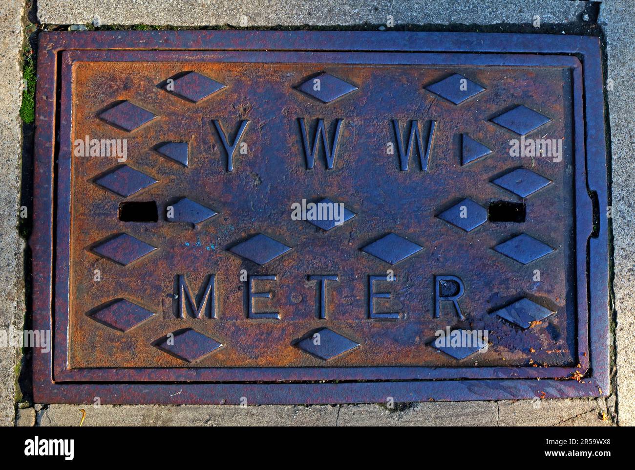 Primo piano di una rete di distribuzione in ghisa contrassegnata con “YWW”, riferita alla York Water Works, che mostra metallo arrugginito e infrastrutture idriche storiche a York Foto Stock