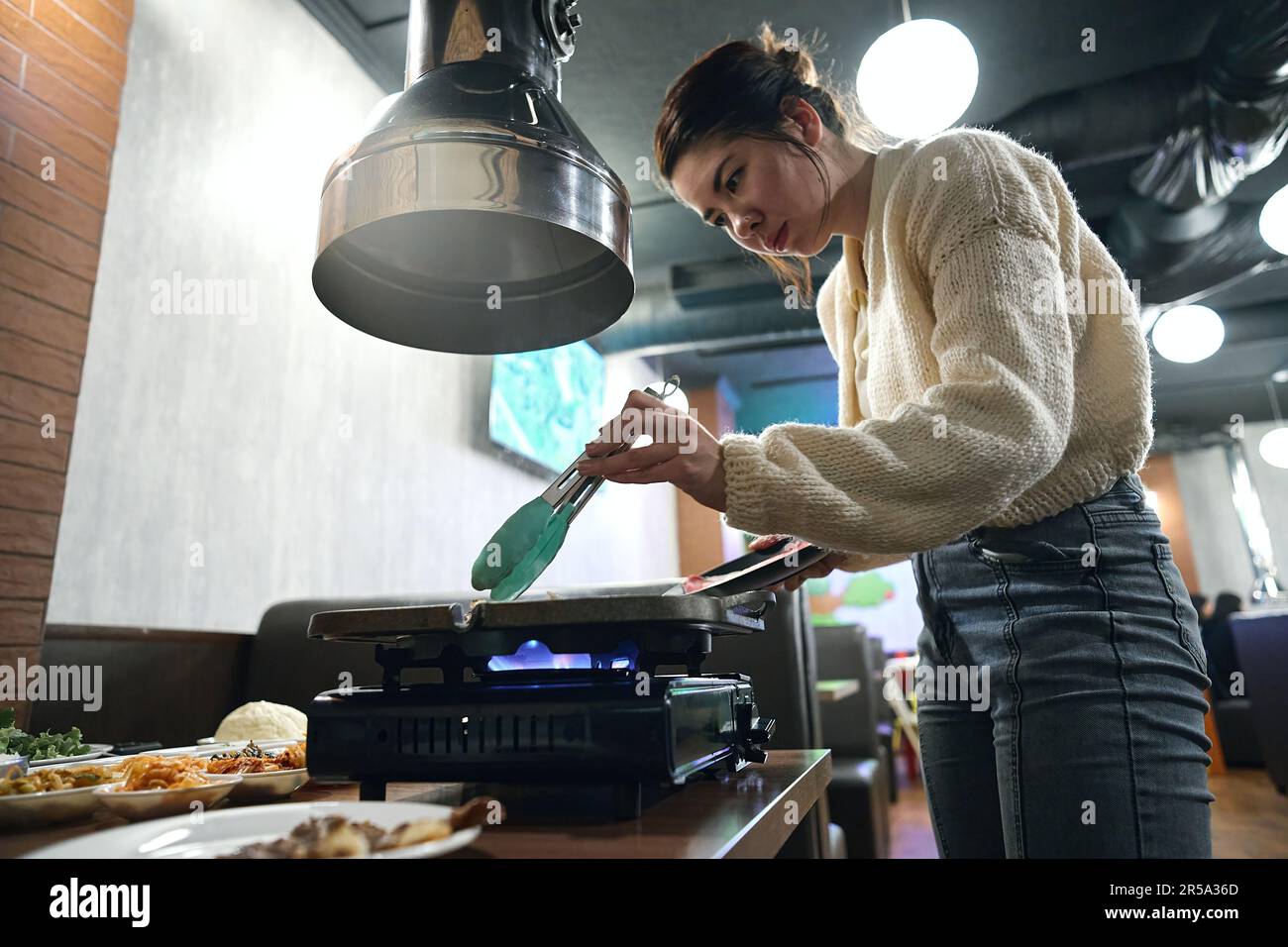 La donna asiatica cucina la carne nella padella sulla stufa nelle regate Foto Stock