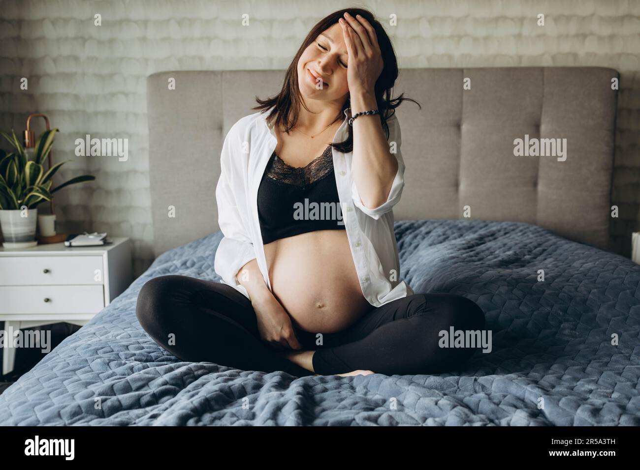 Ragazza incinta seduta sul letto con gli occhi chiusi Foto Stock