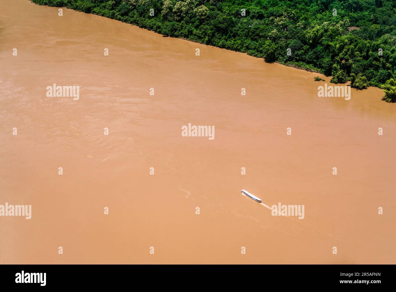 Vista aerea di una barca Slow Boat del Laos che naviga su un bacino inferiore marrone fangoso gonfio del fiume Mekong dopo alte precipitazioni. Foto Stock