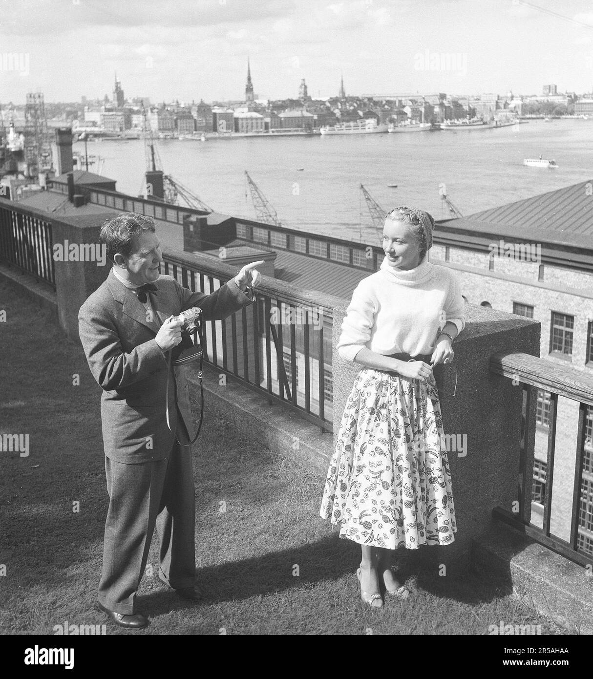 Fotografo amatoriale negli anni '1950s. Un paio di turisti a Stoccolma e l'uomo si alza con la fotocamera e vuole immortalare il suo partner con il flusso di Stoccolma sullo sfondo. È vestita con una gonna d'epoca e un maglione a maglia. È attore americano Burgess Meredith che prende una foto della sua moglie svedese Kaja Sundsten. Svezia 1954. Foto Kristoffersson Ref BF78-1 Foto Stock