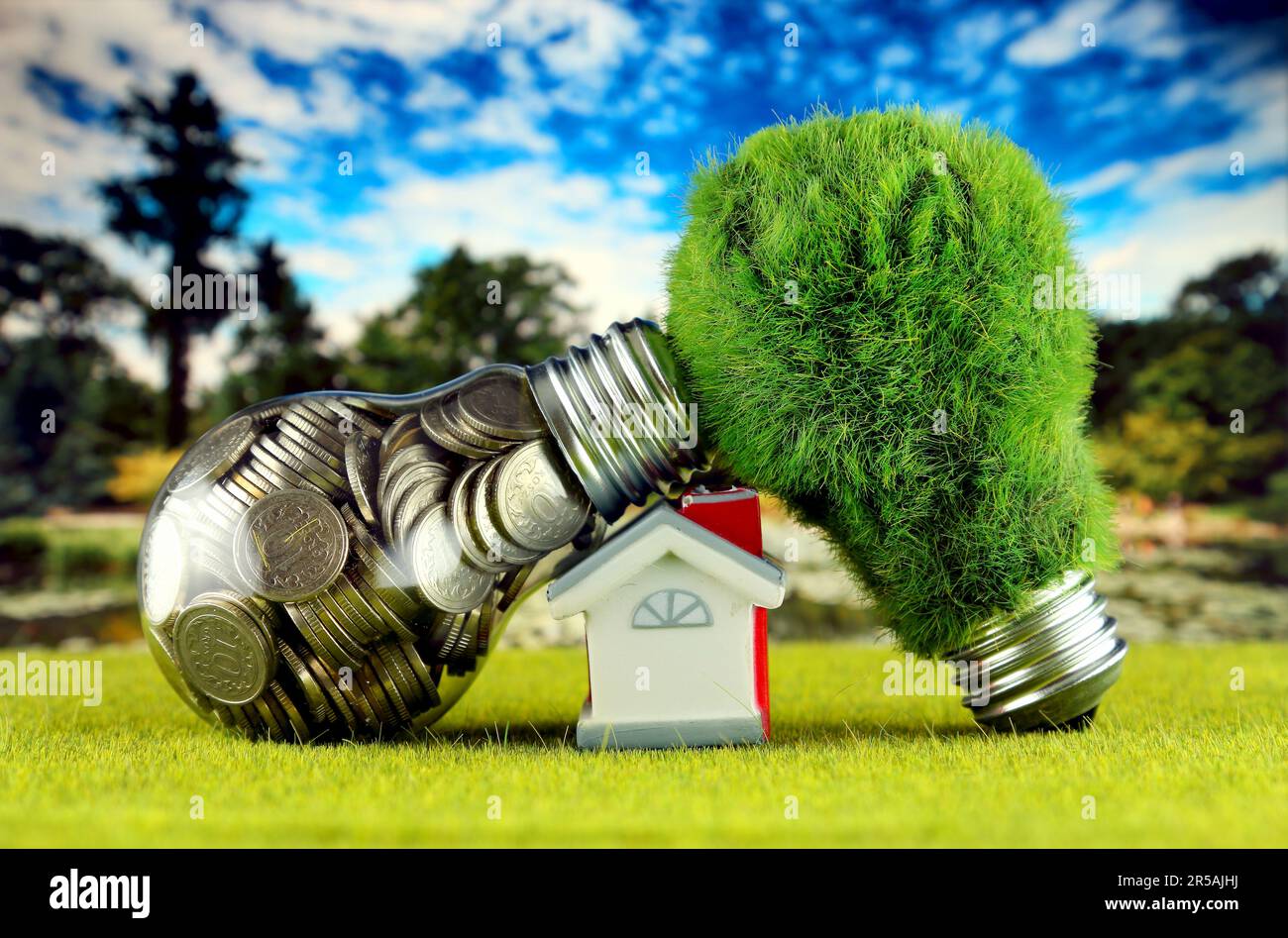 Monete all'interno della lampadina, lampadina verde eco con erba e casa in miniatura. Concetto di energia rinnovabile. I prezzi dell'elettricità, il risparmio energetico nelle ore Foto Stock