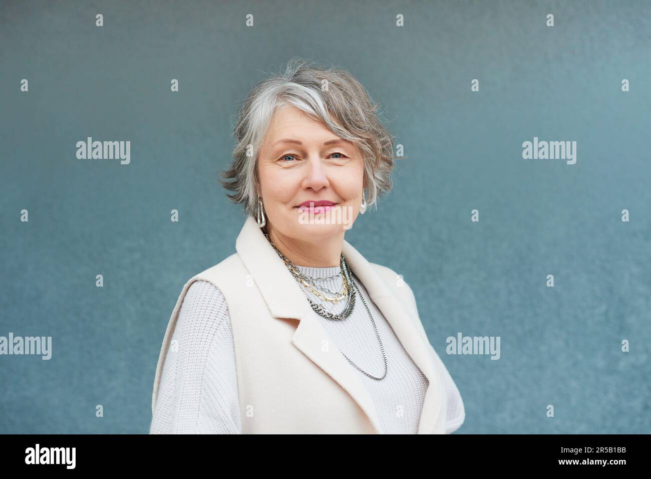 Ritratto all'aperto di bella donna di 55 - 60 anni che posa accanto a parete di sfondo blu Foto Stock