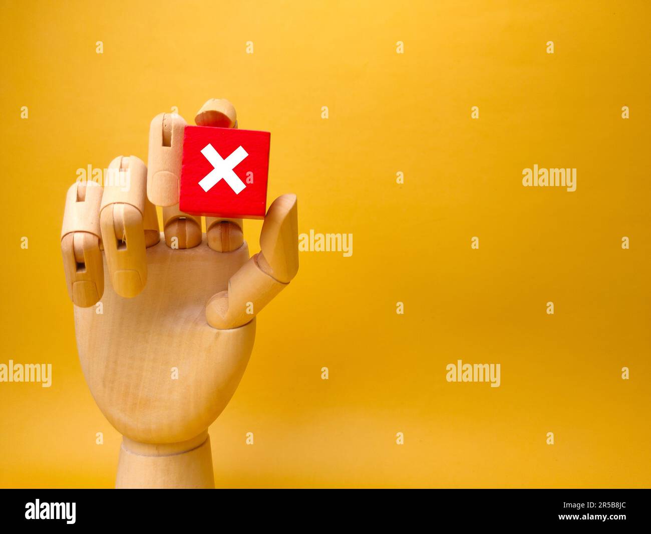 Un primo piano di una mano umana che afferra un oggetto rosso brillante, di forma quadrata con un segno X. Foto Stock