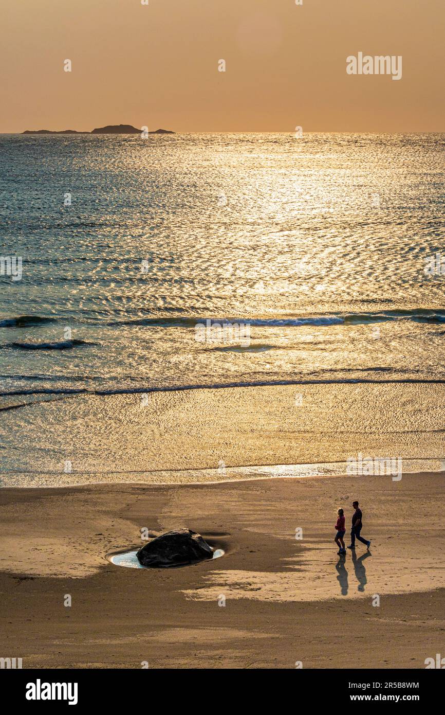 Giovani coppie che camminano al tramonto sulla spiaggia di Whitesands Bay, una spiaggia con bandiera Blu, la penisola di St David, il Pembrokeshire Coast National Park, West Wales Foto Stock