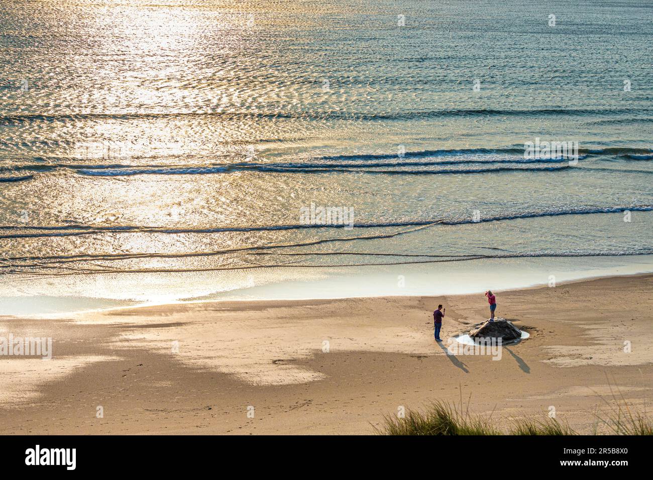 Giovani coppie che camminano al tramonto sulla spiaggia di Whitesands Bay, una spiaggia con bandiera Blu, la penisola di St David, il Pembrokeshire Coast National Park, West Wales Foto Stock
