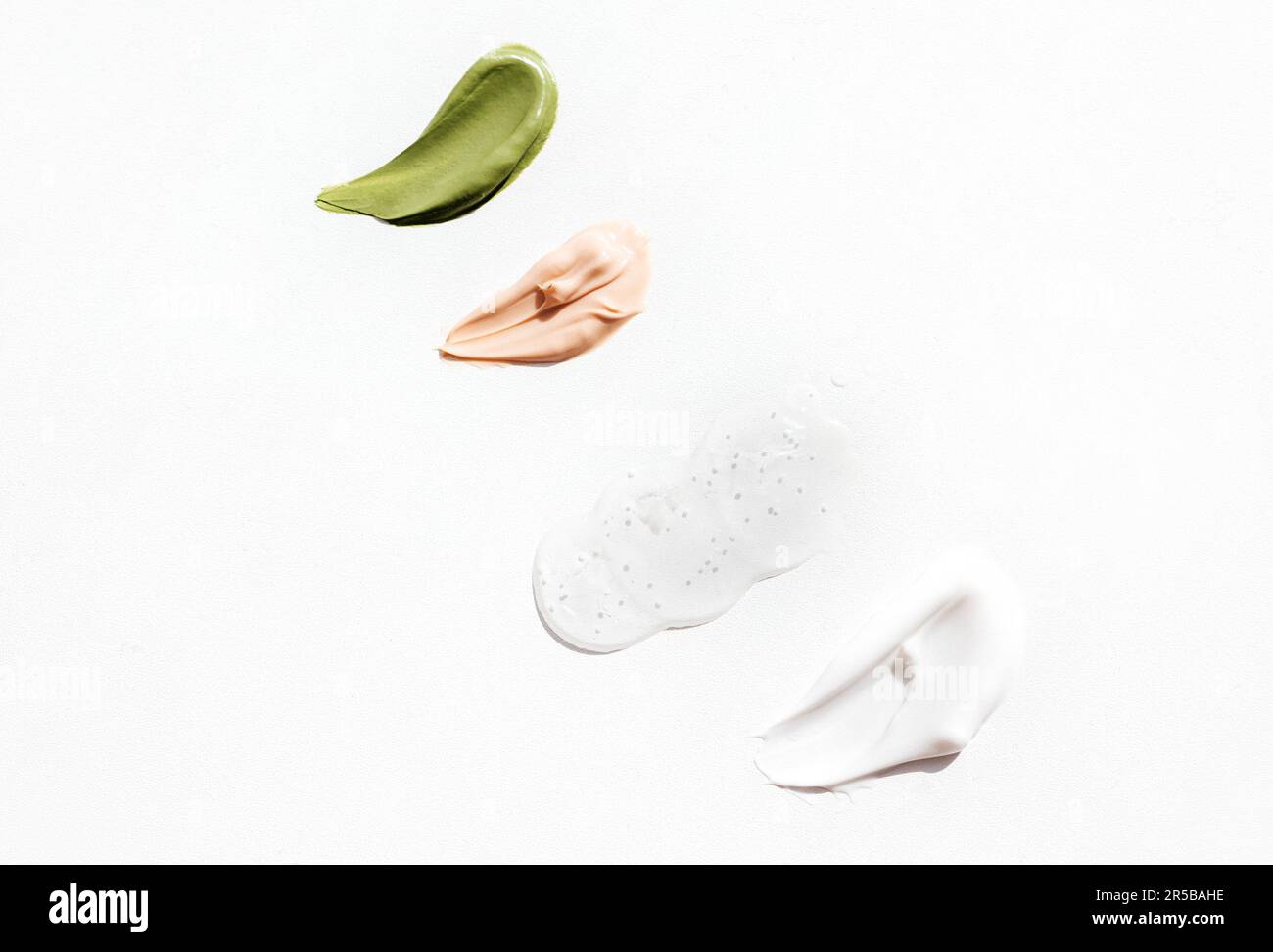 Macchie cosmetiche di colore verde, rosa e bianco crema su sfondo luminoso. Vari strisci di vernice testurizzata di prodotti cosmetici su sfondo bianco. Conce Foto Stock