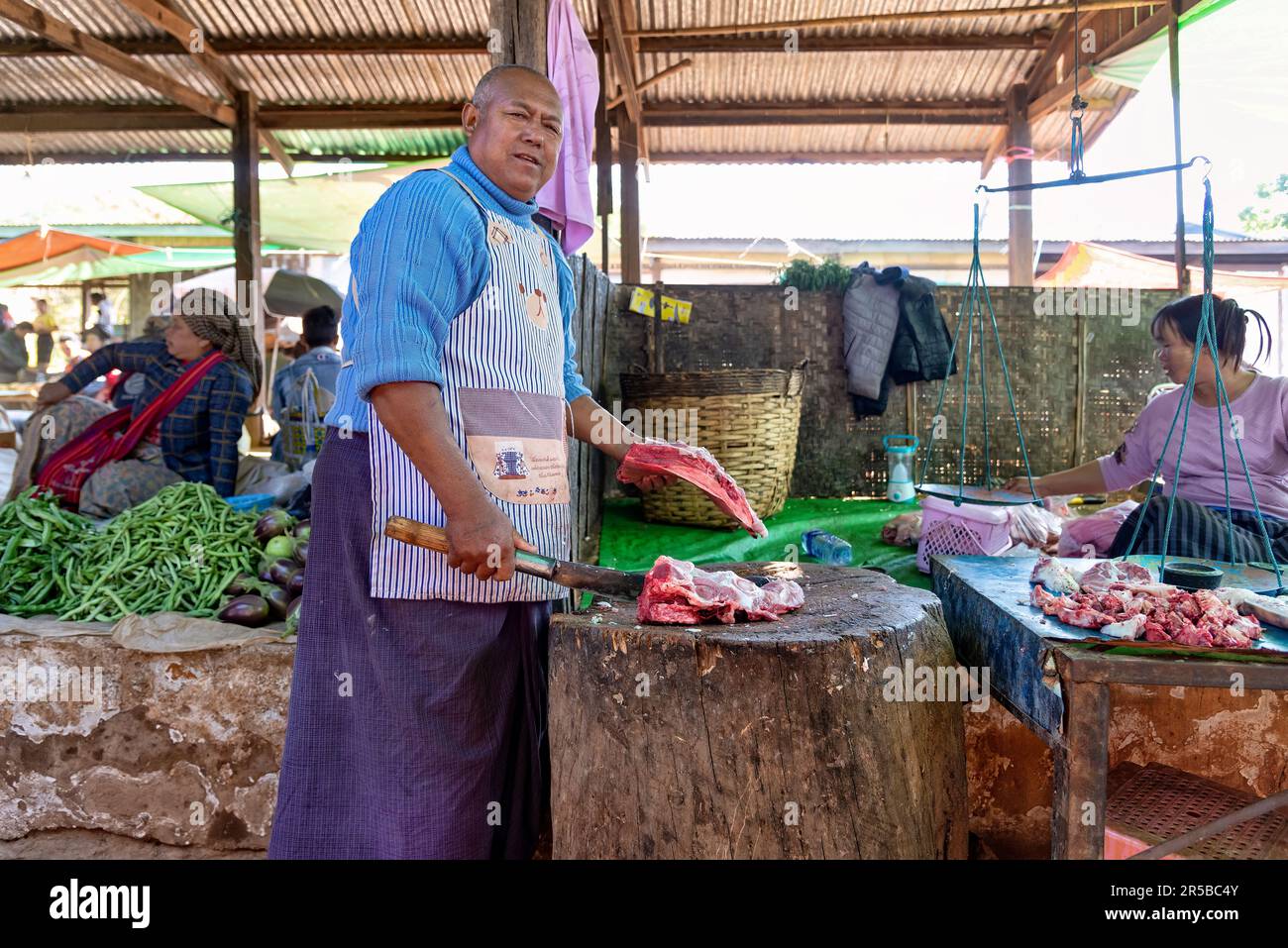 Heho, Myanmar - 26 dicembre 2019: Un macellaio con vestiti colorati al lavoro nel mercato locale. Questo è il mercato più grande della zona Foto Stock