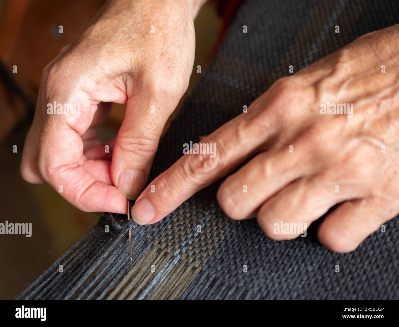 Lavorazione di cuciture sull'estremità del tessuto grigio tessuto. Finitura artigianale della tessitura, focalizzazione selettiva Foto Stock