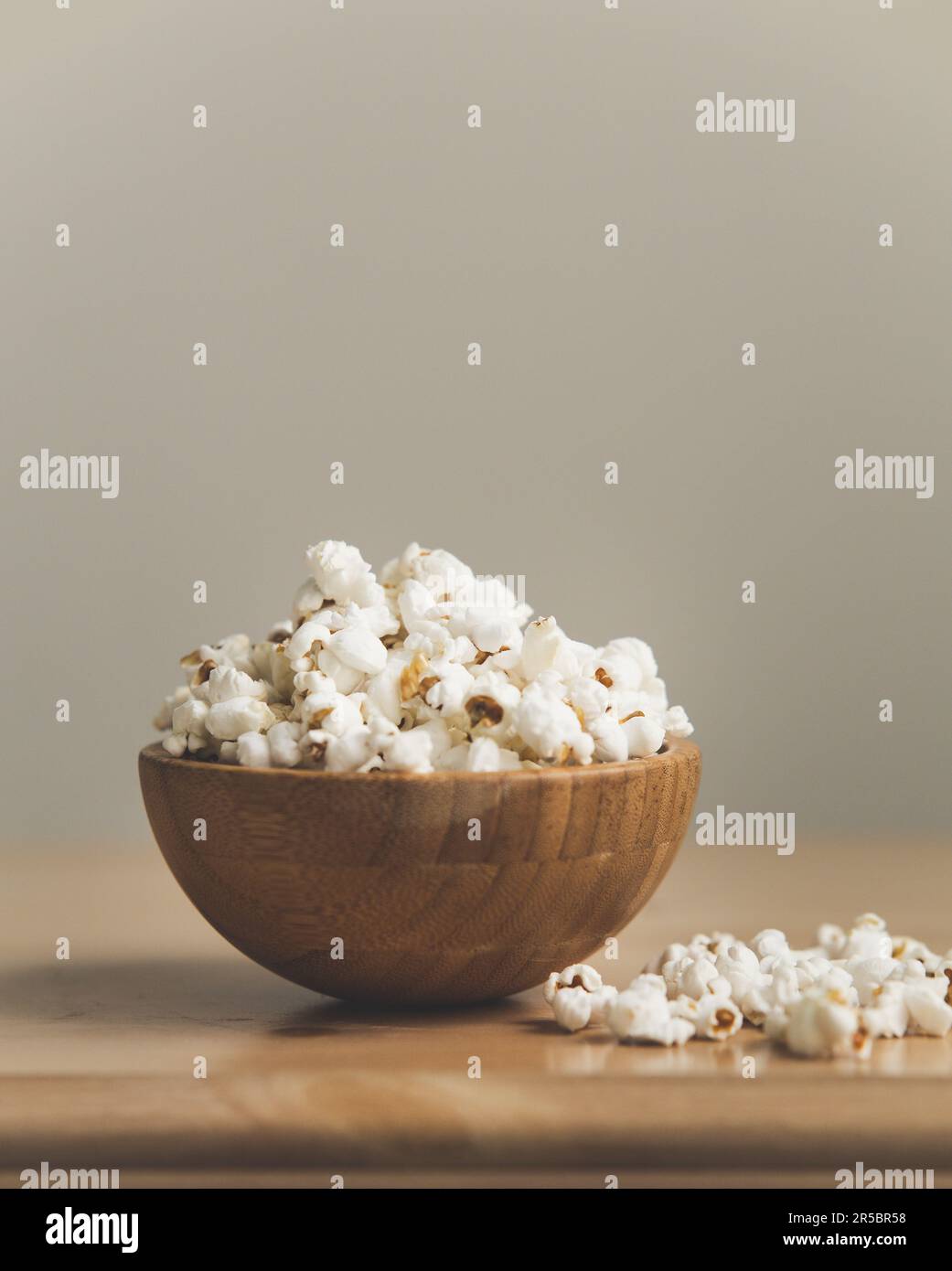 Una ciotola di legno contenente popcorn appena schioccato, con due pezzi di noccioli schioccati sul tavolo Foto Stock
