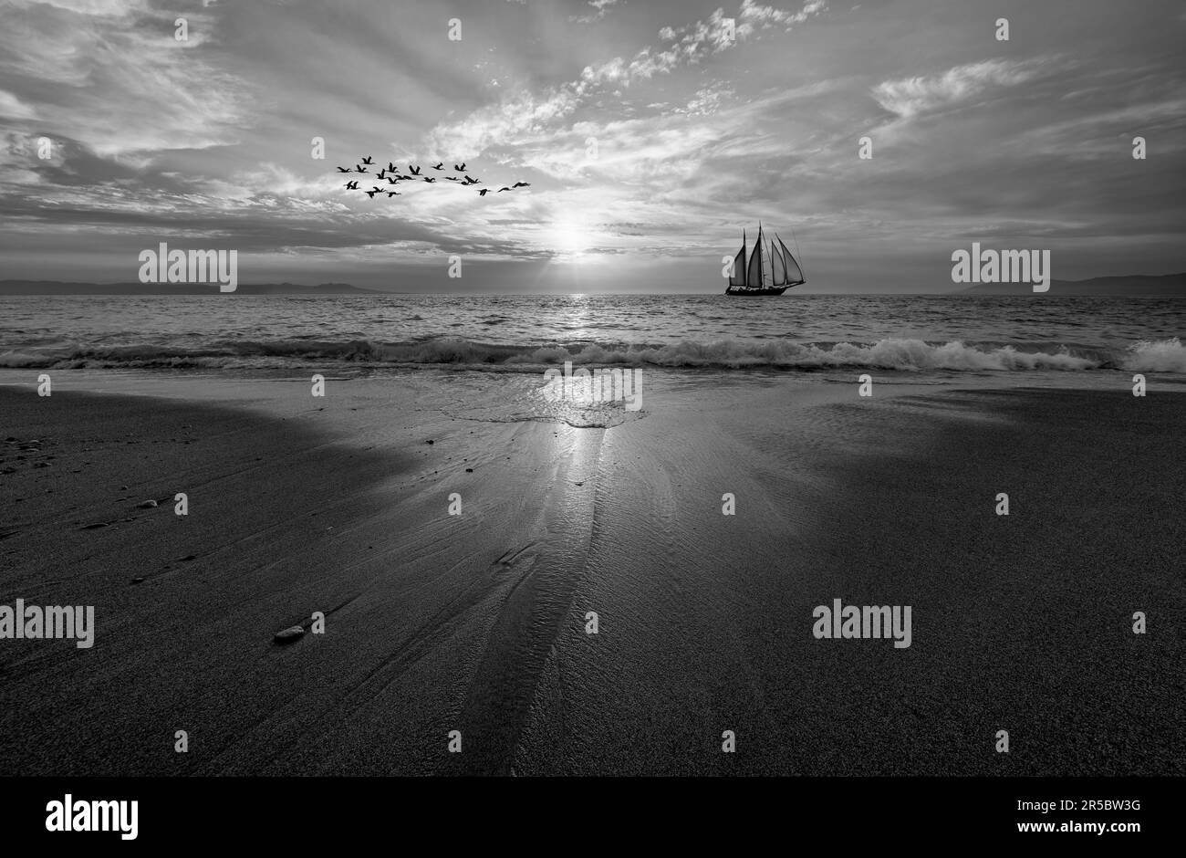 Una barca a vela sta navigando lungo l'oceano con Un'onda che si rompe sulla riva in bianco e nero Foto Stock
