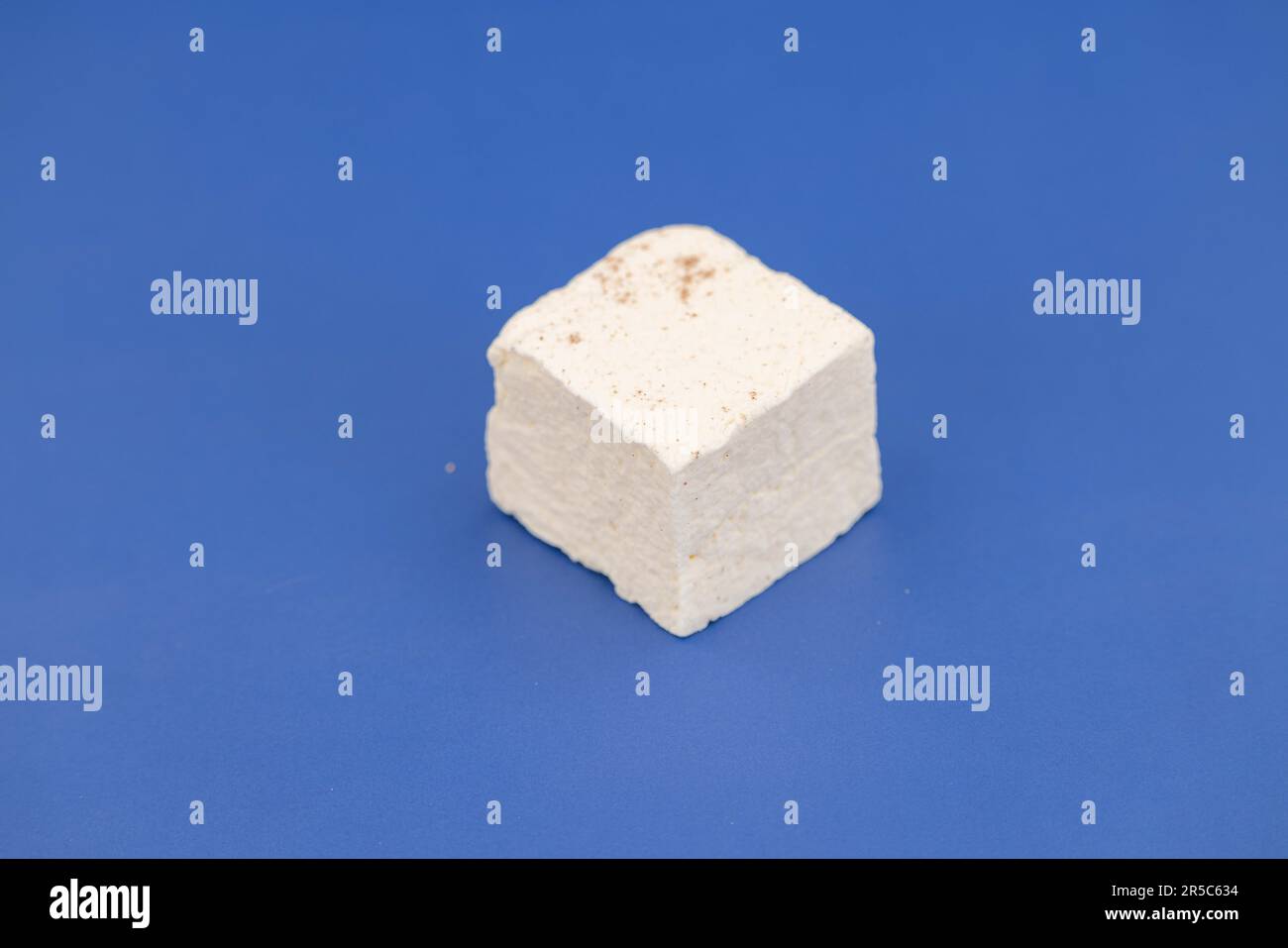 Un cubo bianco di marshmallow è disposto su una superficie piatta blu scuro profondo Foto Stock