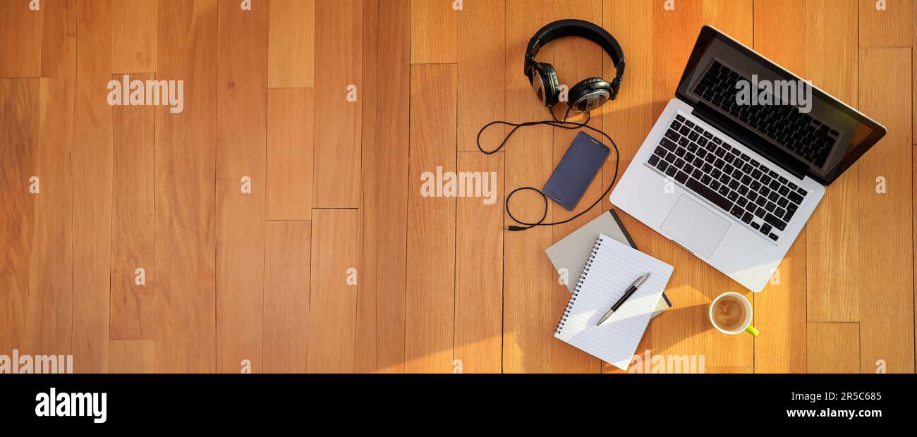 Ufficio domestico, lavoro da casa. Computer portatile, telefono cellulare, cuffie sul pavimento in legno, vista dall'alto Foto Stock