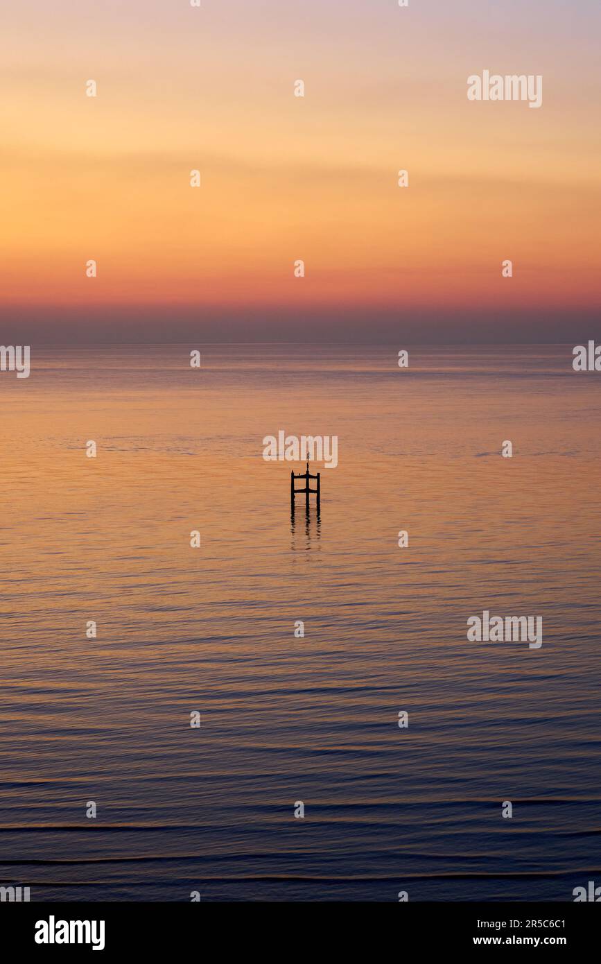 Una vista astratta orientata verticalmente di una struttura in legno in un mare calmo all'alba Foto Stock