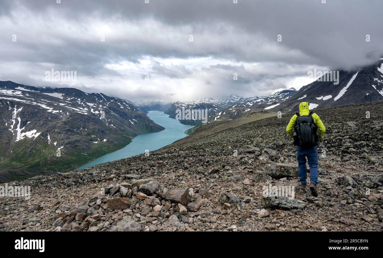 Arrampicatori su sentiero roccioso, escursione Besseggen, passeggiata sul crinale, vista sul lago Gjende e sulle montagne innevate, Parco Nazionale di Jotunheimen, Vaga, Innlandet, Norvegia Foto Stock