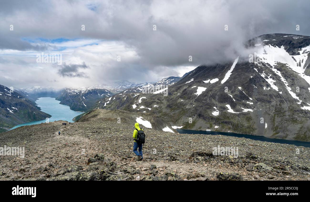 Arrampicatori su sentiero roccioso, escursione Besseggen, passeggiata sul crinale, vista sul lago Gjende e sulle montagne innevate, Parco Nazionale di Jotunheimen, Vaga, Innlandet, Norvegia Foto Stock