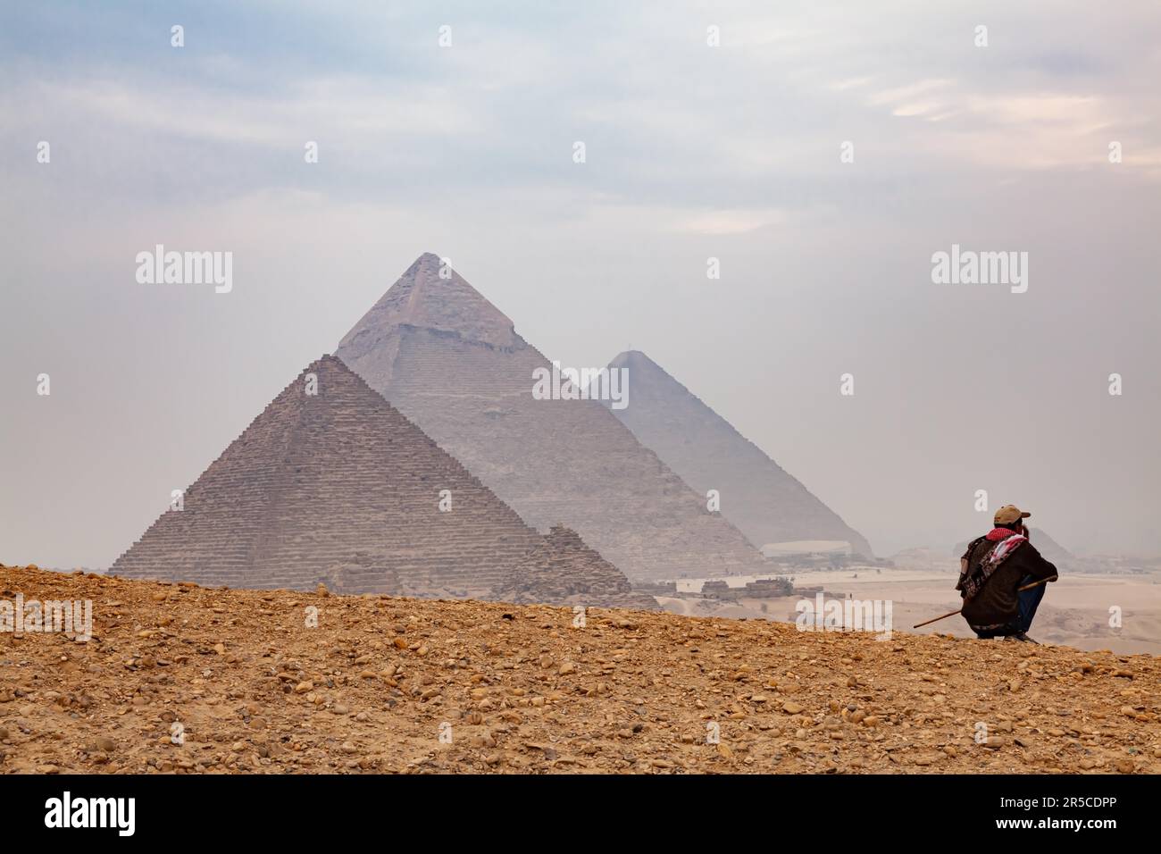 Cairo, Egitto - 30 dicembre 2011 : Egiziano seduto su una collina con le piramidi sfocate sullo sfondo dell'altopiano di Giza in un giorno di nebbia, il Cairo Foto Stock